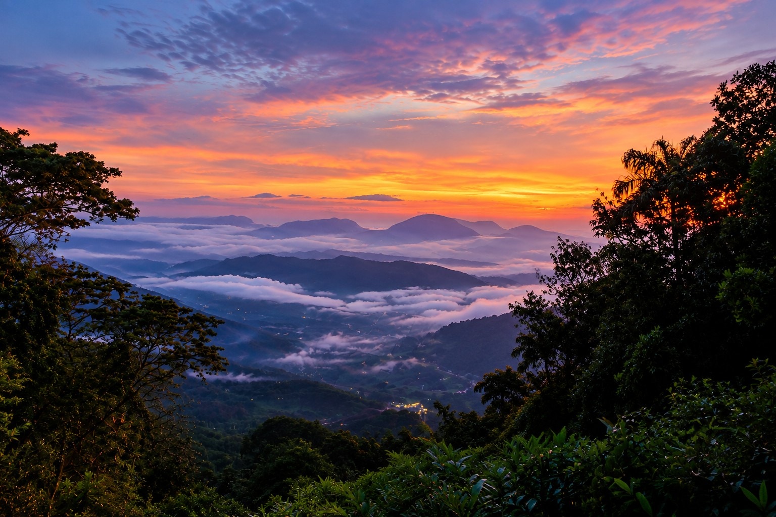Misty mountain valley at sunset with layered peaks, clouds, and lush green forest